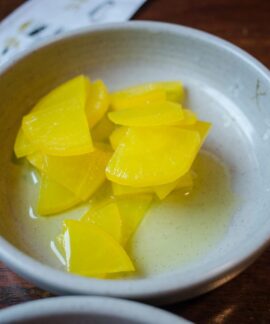 Close-up of sliced yellow pickled daikon radish in a ceramic bowl.