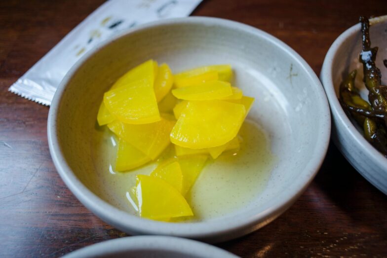 Close-up of sliced yellow pickled daikon radish in a ceramic bowl.