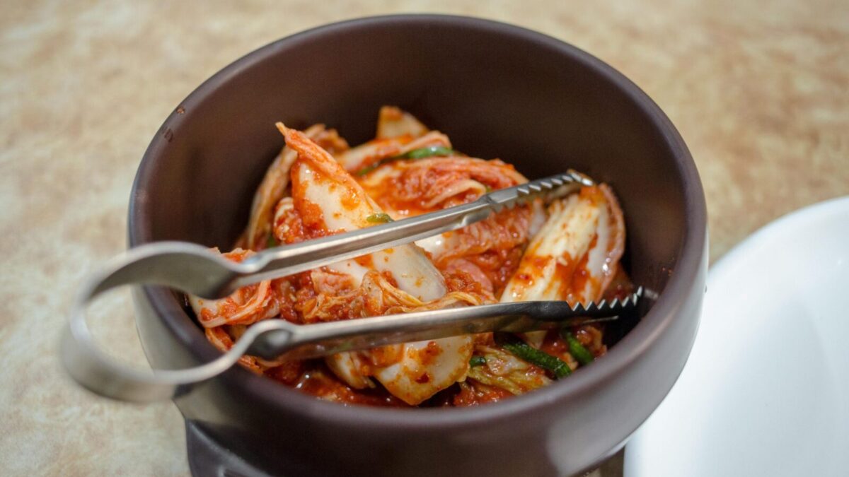 Close-up of traditional Korean kimchi in a dark ceramic bowl with tongs.