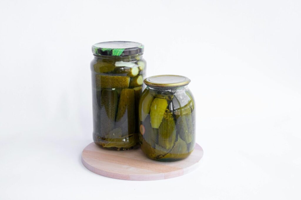 Two jars of pickles sit on a wooden board, showcasing preserved cucumbers in a still life composition.