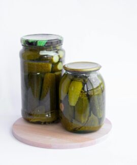 Two jars of pickles sit on a wooden board, showcasing preserved cucumbers in a still life composition.