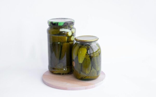 Two jars of pickles sit on a wooden board, showcasing preserved cucumbers in a still life composition.
