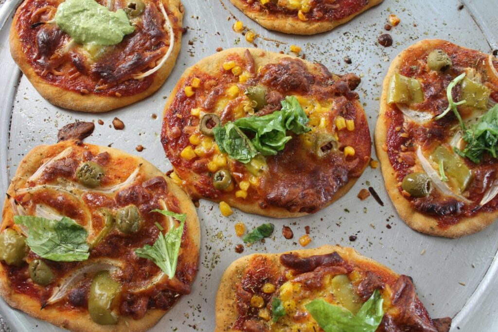 Close-up of assorted pizzettas with toppings like olives and basil on a baking tray, emphasizing their deliciousness.