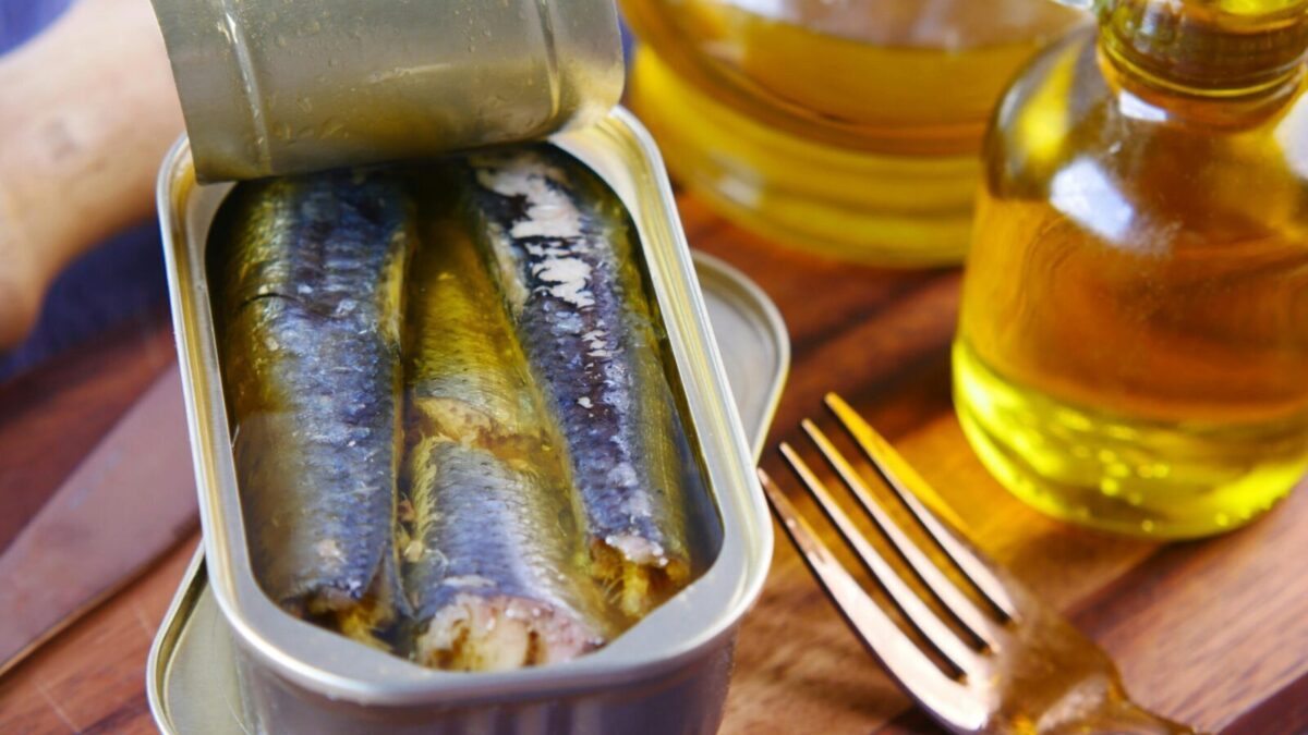 Close-up of canned sardines in olive oil with a fork on a wooden surface.