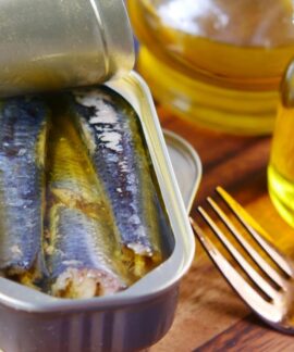 Close-up of canned sardines in olive oil with a fork on a wooden surface.