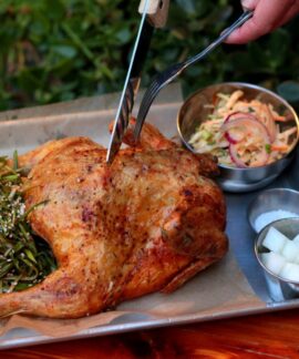 A delicious roasted chicken served with sides and a refreshing beer, captured outdoors.
