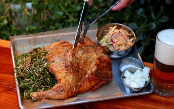A delicious roasted chicken served with sides and a refreshing beer, captured outdoors.