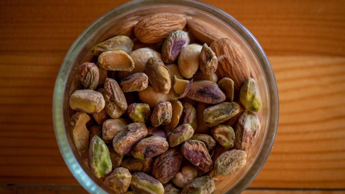 A close-up top view of assorted nuts in a glass bowl on a wooden table, highlighting natural textures.