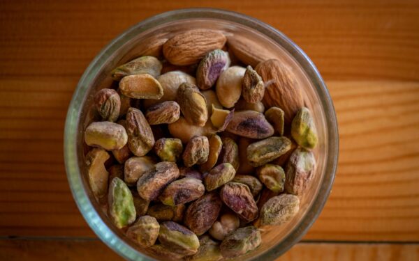 A close-up top view of assorted nuts in a glass bowl on a wooden table, highlighting natural textures.