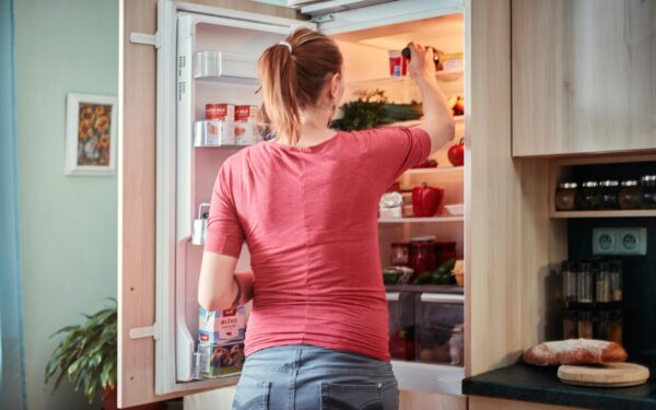 A woman opens the fridge to retrieve food items in a cozy kitchen setting.