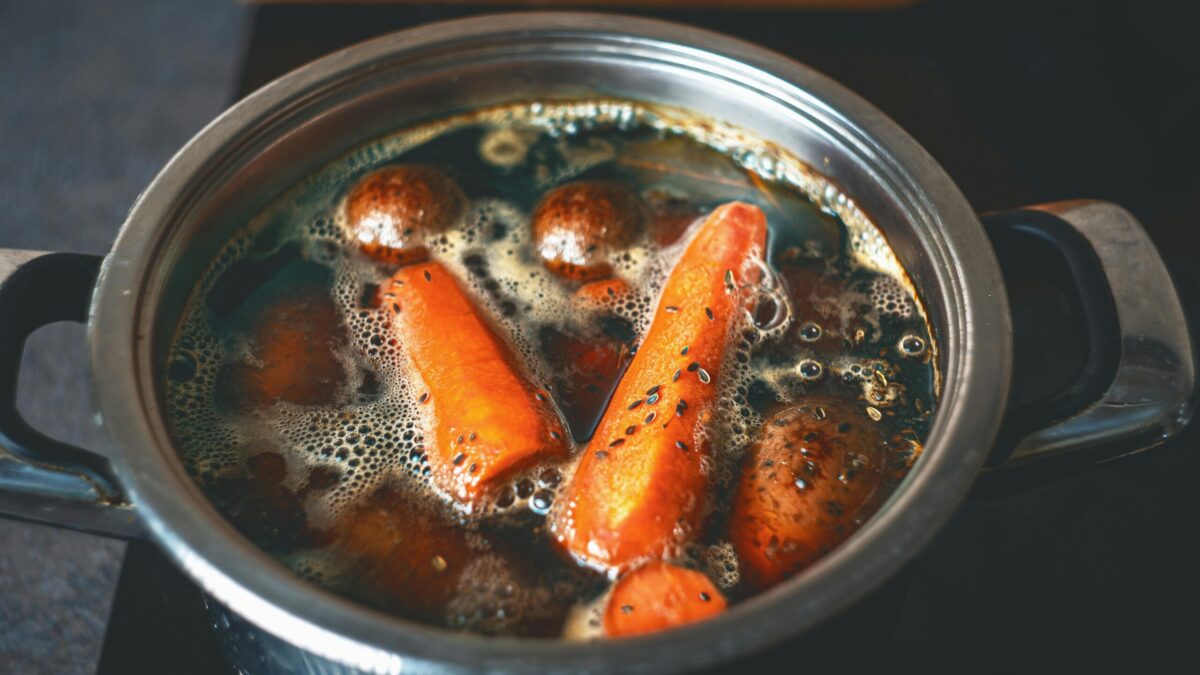 A close-up of carrots and potatoes boiling in a metal pot on a stove.