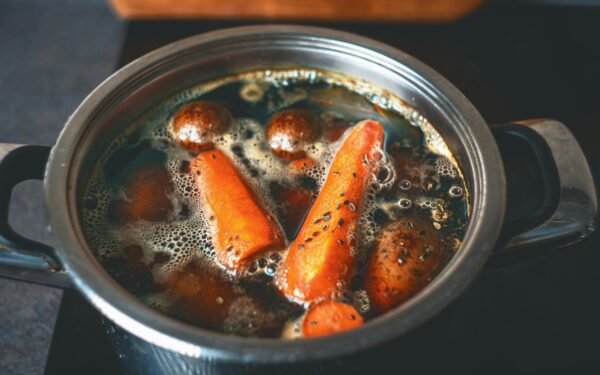 A close-up of carrots and potatoes boiling in a metal pot on a stove.