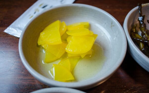 Close-up of sliced yellow pickled daikon radish in a ceramic bowl.