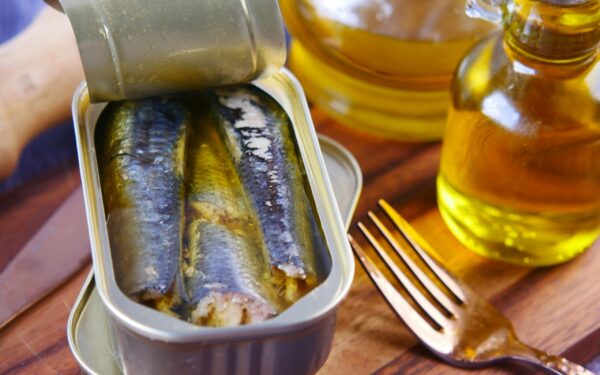 Close-up of canned sardines in olive oil with a fork on a wooden surface.