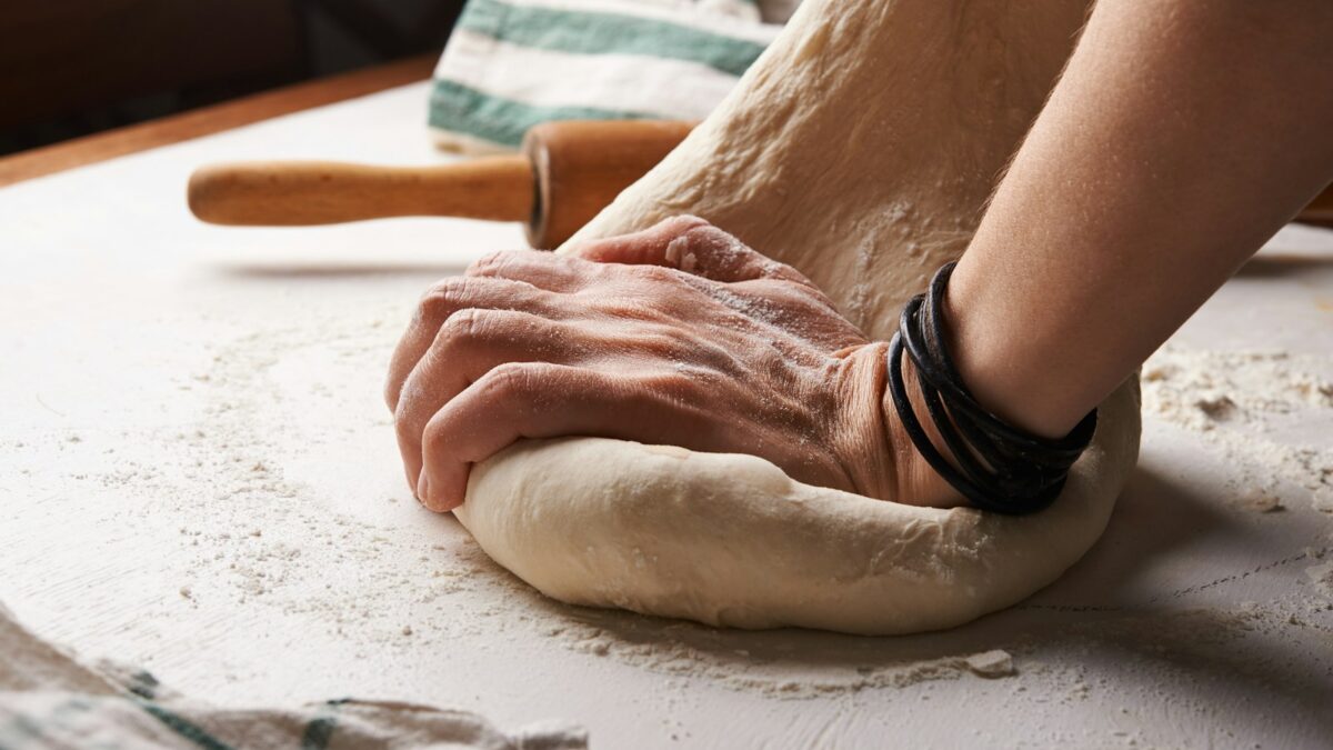 person making dough beside brown wooden rolling pin