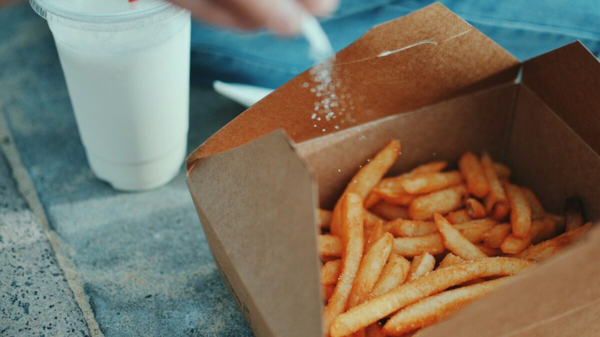person sprinkling salt in fries