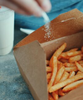 person sprinkling salt in fries