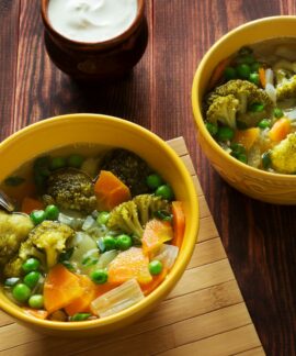 two bowls of soup with peas, carrots and broccoli