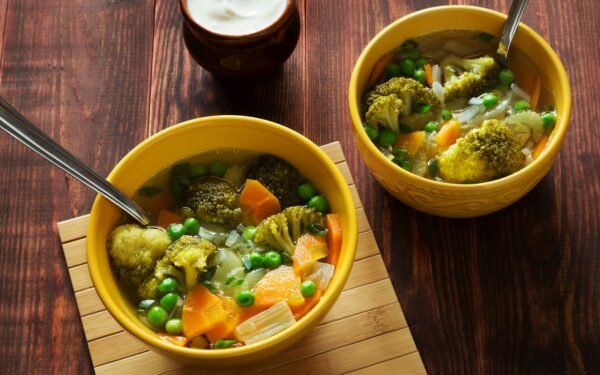 two bowls of soup with peas, carrots and broccoli