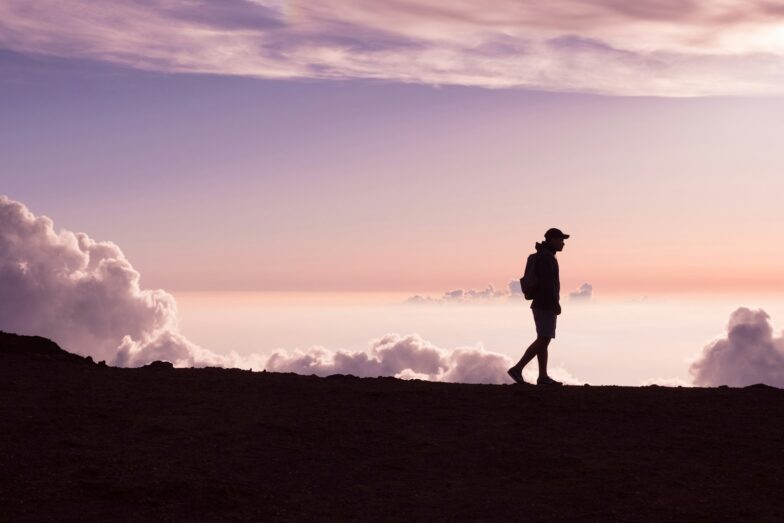 silhouette of person walking under white clouds