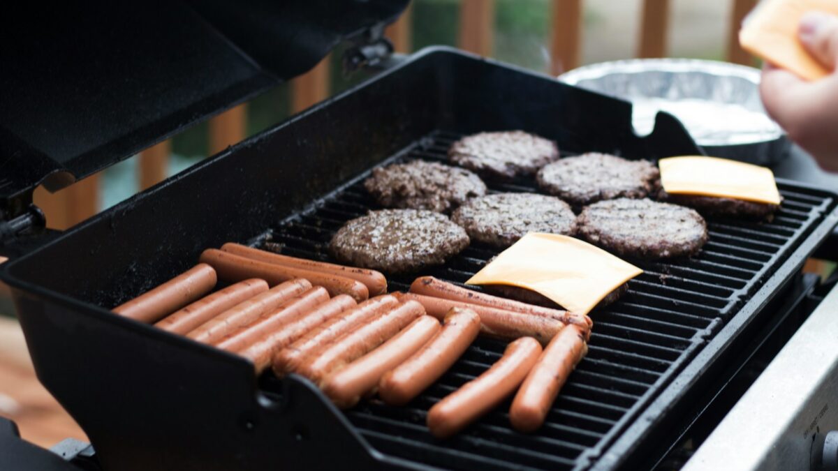 person standing in front grill grilling sausage