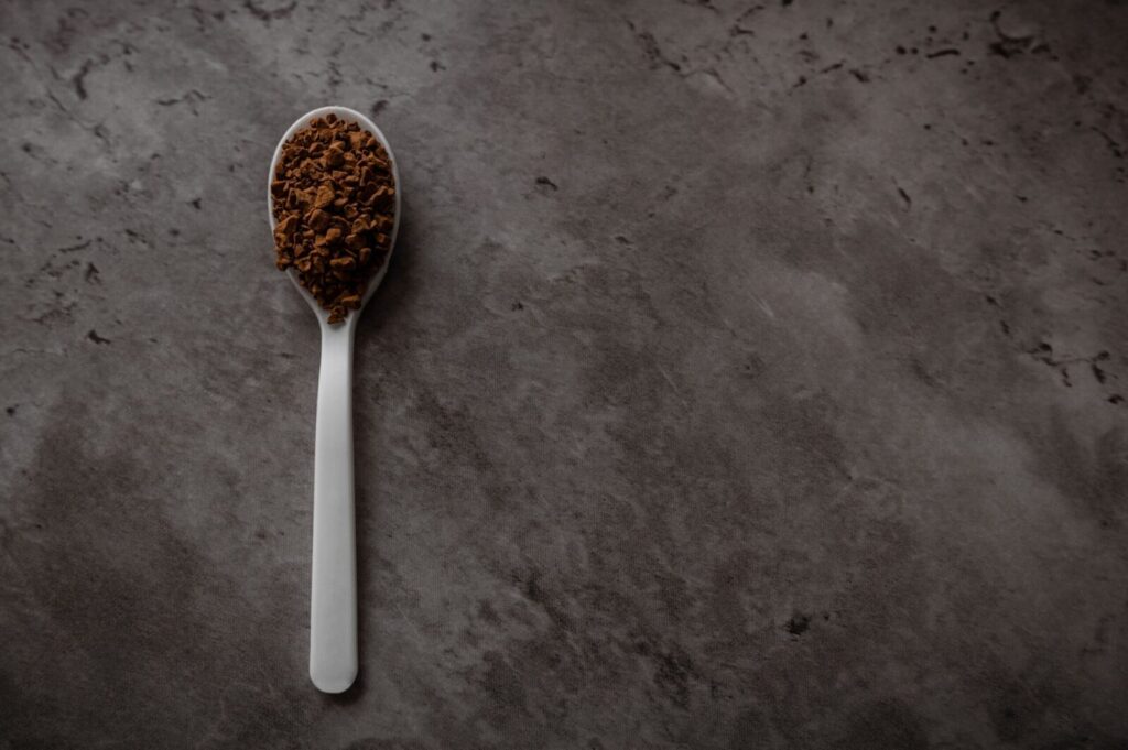 A spoon filled with instant coffee on a dark textured background, perfect for beverage themes.