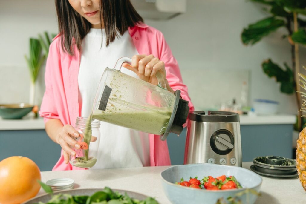 Woman making nutritious green smoothie in kitchen with fruits and vegetables.
